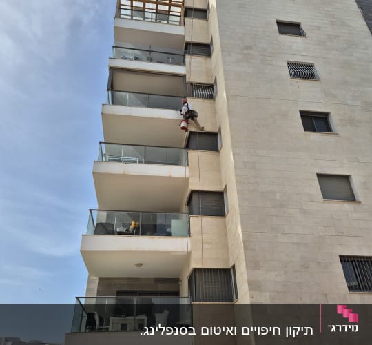 אדם תלוי על חבל צובע קיר חיצוני של בניין